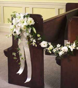 This pew bow contains white lilies, white delphinium, white 	orchids, white lisianthus, variegated ivy, greens and white satin 	ribbon.
